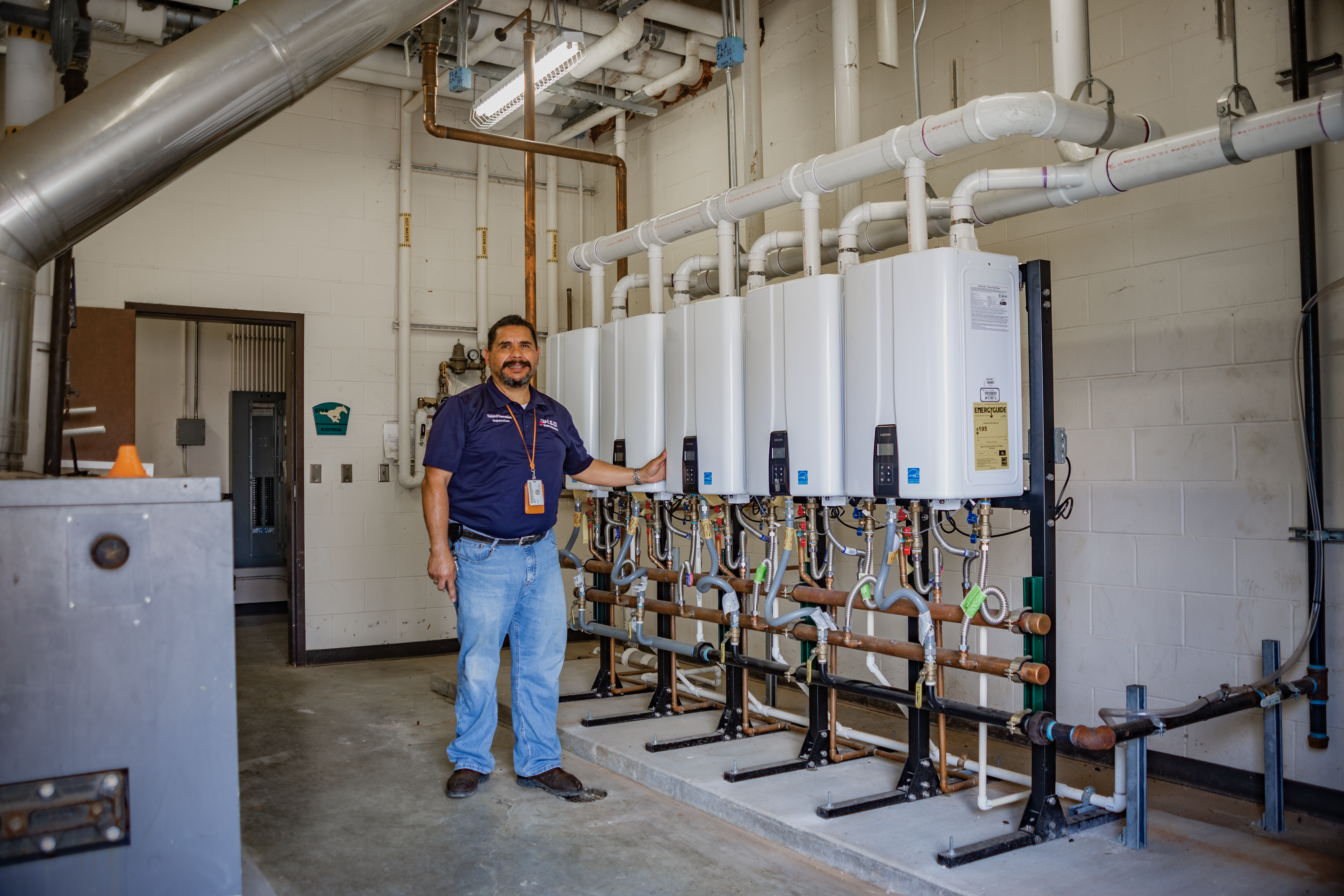 Master Plumber Roland Gonzales alongside Navien tankless water heater installation in high school fieldhouse